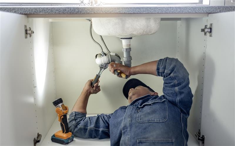 Plumber repairing pipes beneath a bathroom sink in Colorado Springs