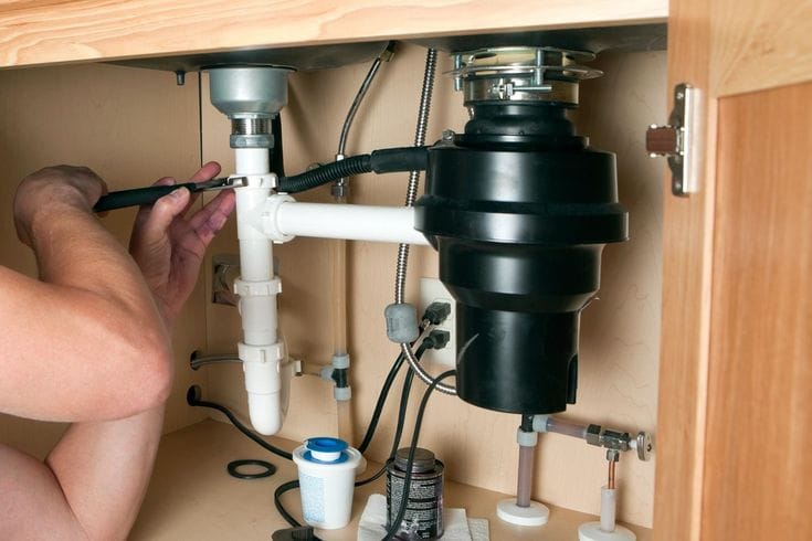 Plumber installing a garbage disposal beneath a kitchen sink in Colorado Springs