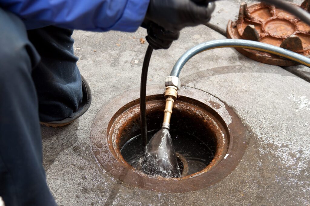Plumber hydro jetting a sewer line through a manhole in Colorado Springs