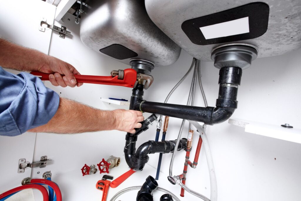 Plumber repairing drain pipes beneath a kitchen sink in Colorado Springs